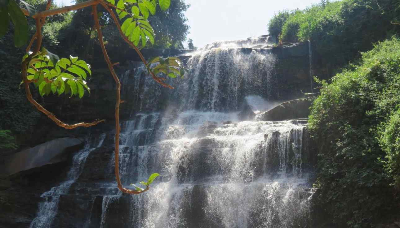 Waterfall in Ghana surrounded by lush green vegetation and bright sunlight, nature tour at Timeh Tours.